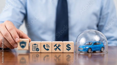 Business person placing wooden block with car shield icon next to toy car under glass dome with man shirt tie