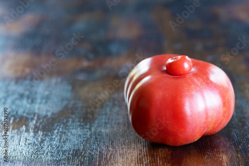 Ripe and red unusual ugly tomato with small tomato growing naturally on top of its larger body, creating strikingly irregular form, on rustic wooden surface. Concept for imperfect produce