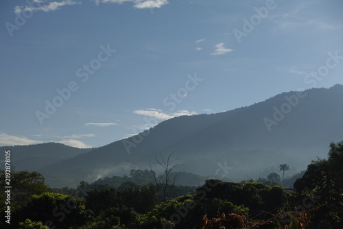 Foto view of multiple layers of hazy, dark mountains receding into the distance under a light blue sky with scattered wispy clouds