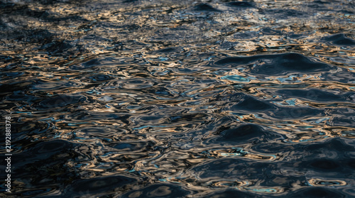 Abstract water ripples with golden sunset reflections on a dark liquid surface