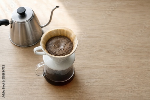 Pour over coffee maker with blooming grounds and a stainless steel gooseneck kettle preparing a fresh morning brew on a wooden table