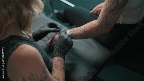 Tattoo artist prepares a clients forearm for a tattoo procedure, working with a stencil while wearing black protective gloves in a professional tattoo studio.