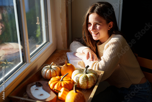 Teen girl relaxing by window with decorative pumpkins at home