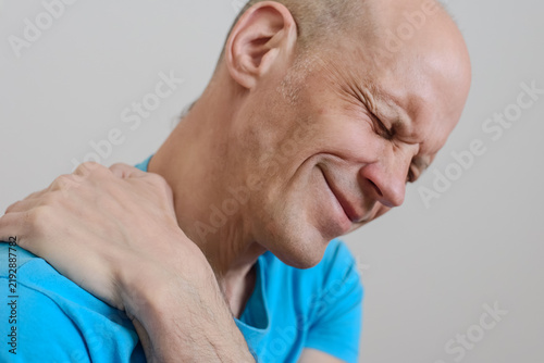 Tired man massaging stiff sore neck and suffering from muscle ache Facial expression illustrating acute neck pain during everyday activities