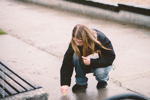 Fotografie Young blonde girl squatting and drawing with colorful chalk on the pavement in a