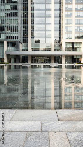 Modern Corporate Plaza with Reflective Fountain Pool Showing Concentric Water Ripples and Glass Office Buildings Reflection on Overcast Day, Urban Architecture