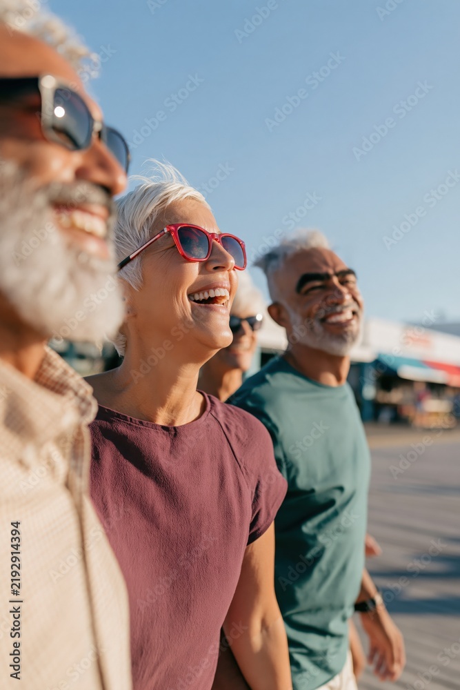 Fototapeta premium Smiling senior friends walking on boardwalk background for lifestyle banner and travel poster design