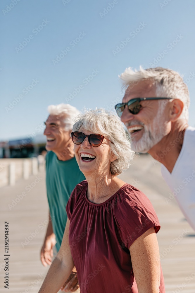 Fototapeta premium Three happy seniors laughing on boardwalk background for retirement lifestyle banner and travel poster
