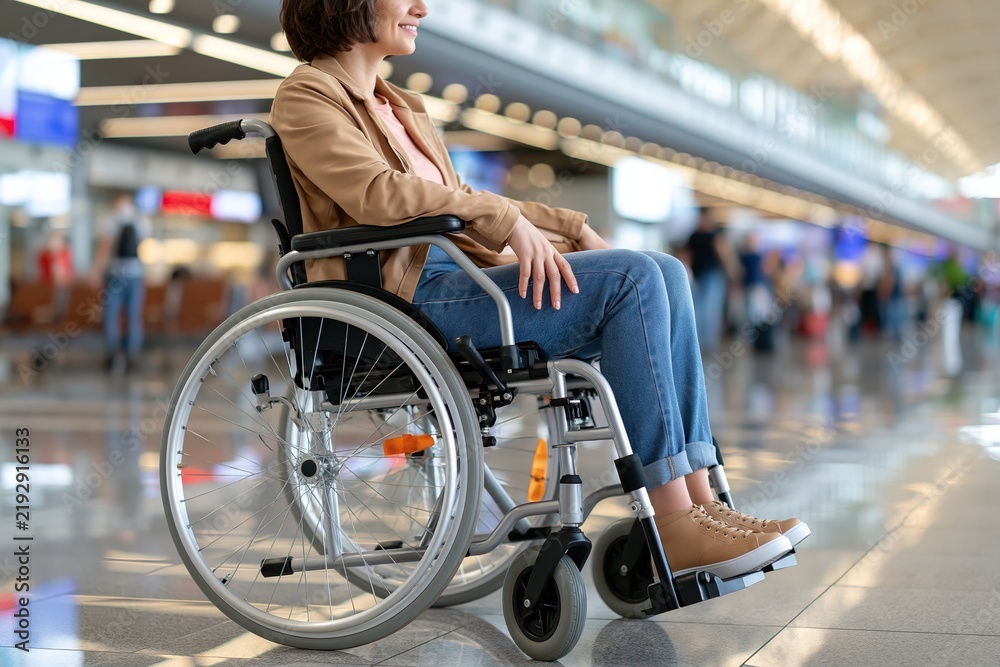 Obraz premium Woman in Wheelchair Navigating a Modern Airport Terminal with Passengers in Background