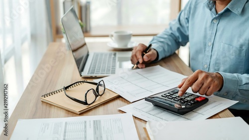 Man calculating finances with calculator and laptop during daytime at desk