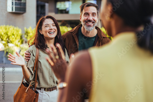 Obraz na plátne Happy Couple Reuniting With Friend On Urban Street Greeting With Warm Smiles And