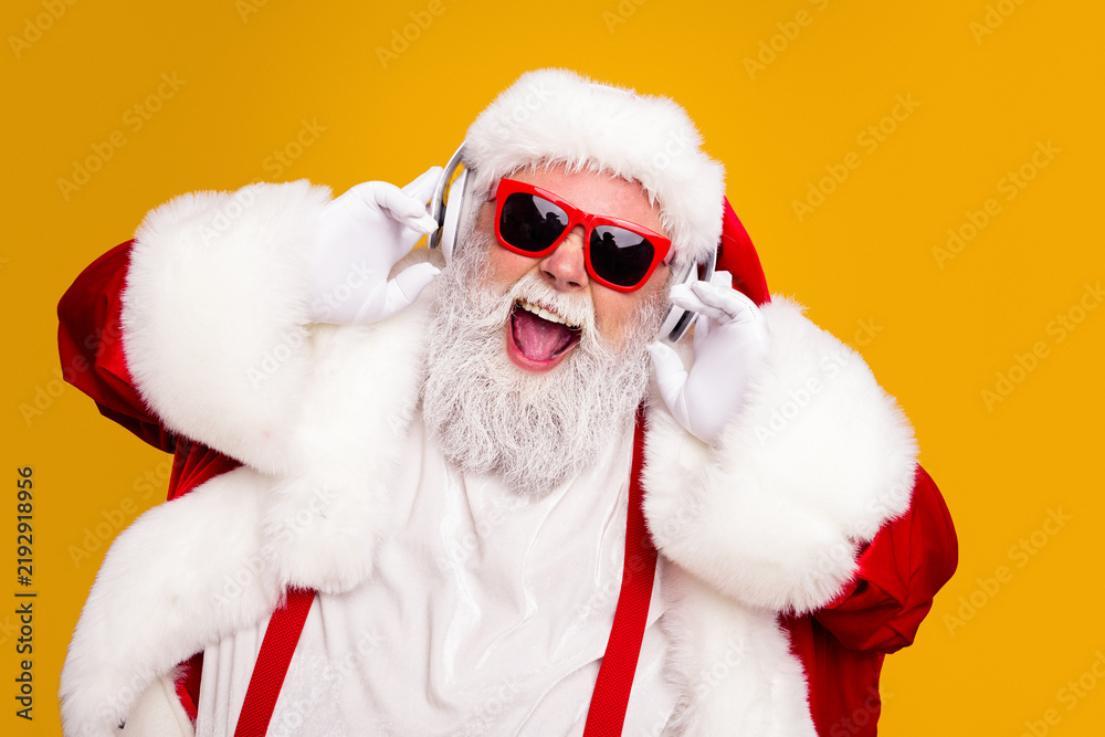 Obraz premium Santa Claus wearing red sunglasses and headphones laughing and enjoying festive Christmas music in a bright studio portrait for holiday advertising and seasonal celebrations