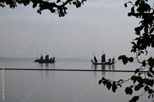 Obraz na plátne Traditional Sailing Boats on Calm Water Framed by Tree Branches