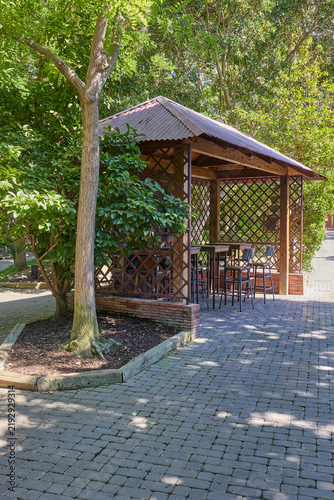 Quadro su tela Wooden gazebo with seating surrounded by lush tropical trees and plants