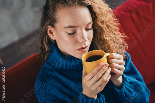 Obraz na plátně Young woman with curly hair enjoying a warm drink in a cozy knitted sweater whil