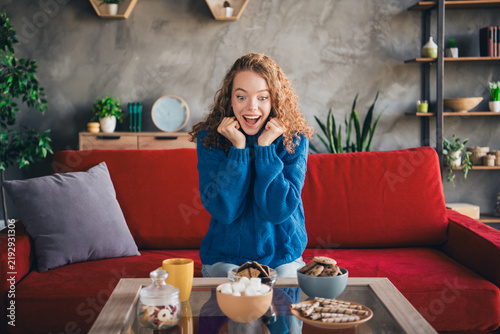 Foto Young woman in a blue knitted pullover expressing joy while sitting in a cozy li