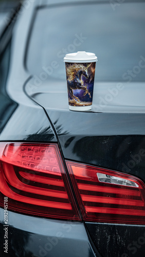 Cup placed on the trunk of a black car with a colorful design in a parking area during daytime