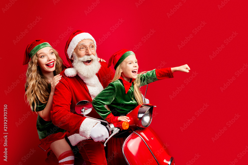 Naklejka premium Santa with two cheerful helpers riding a red scooter celebrating Christmas joy and family fun with elves and holiday excitement