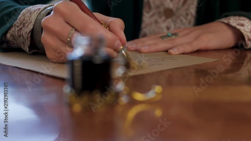 The girl is holding a pen with ink and writing a letter. The girl writes the letter in handwritten font. signing the document. 
