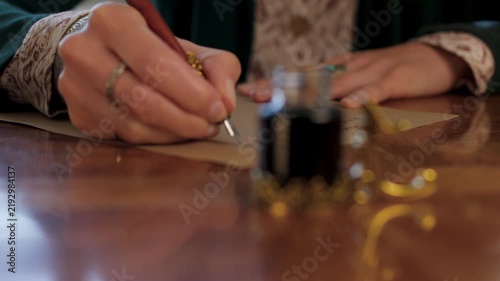 An antique young woman in a resurgent dress, sitting at the table and writing a letter with a vintage pen on an old paper sheet of parchment. The girl is writing a letter in handwritten script. 
