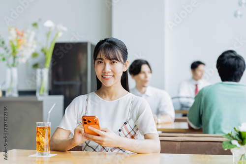 Naklejka カフェでスマホを使う若い女性