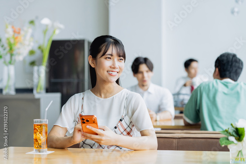 Naklejka カフェでスマホを使う若い女性