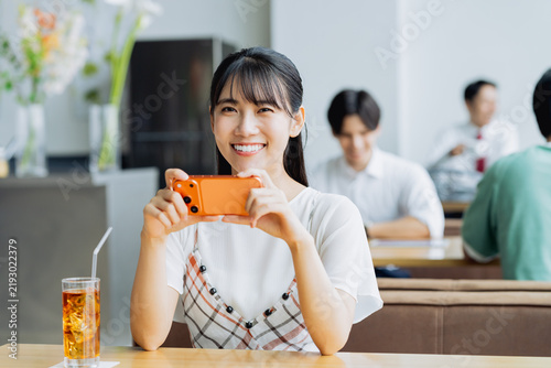 Naklejka カフェでスマホを見る若い女性