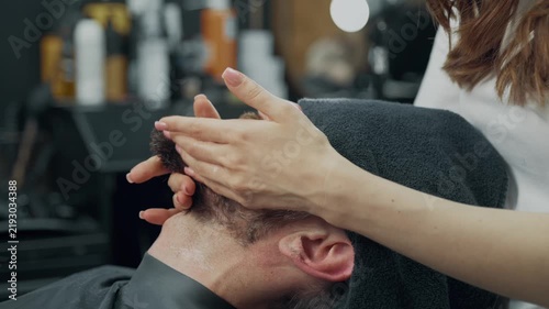 Barber applies lotion to a male clients beard during a professional grooming treatment in a barbershop.