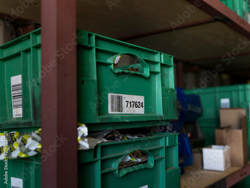 A barcode label on a green plastic crate identifies parts in a shipyard storeroom, inventory tracking in an industrial supply chain.