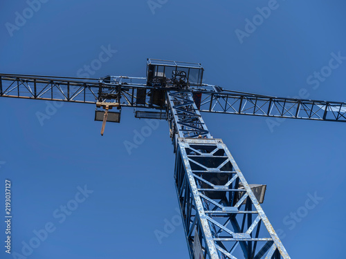 Fotografie Looking straight up at the jib and trolley of a lattice tower crane, steel framework crossing a cloudless sky