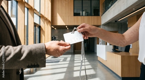 Man receiving blank ID badge from woman at office reception. Visitor getting access card with lanyard in modern building lobby. Business check-in and corporate security concept.
