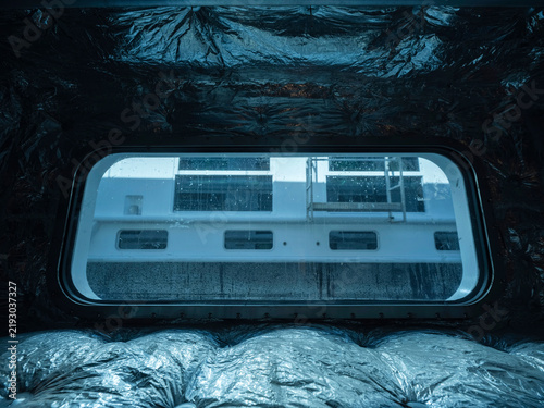 Konstfotografi Reflective insulation frames a ship's window looking out at the white superstructure of the vessel alongside