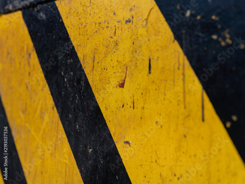 Scratched yellow and black diagonal stripes fill the frame, an abstract industrial pattern of caution markings.
