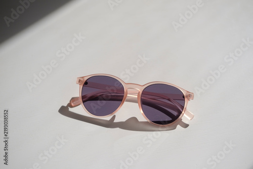Sunglasses placed on a light surface, fashion accessory for sunny days, modern eyewear with rounded pink frames and dark lenses, minimalist lifestyle prop for editorial shoots