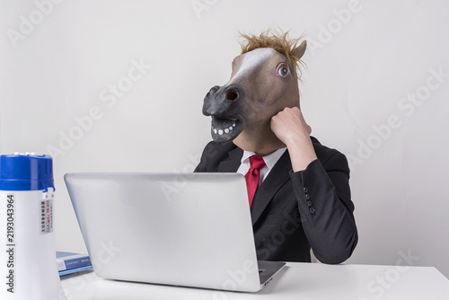 фотографія Businessman Wearing Horse Head Mask Working on Laptop at Desk