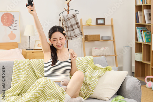 Fotografie Excited young woman celebrating victory with smartphone in cozy living room