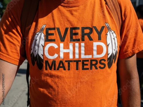 Person wearing orange shirt with every child matters text and eagle feathers for cultural awareness