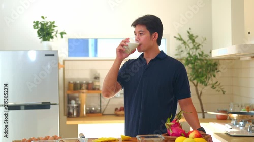 Young Asian Man Holding Glass of Milk in Modern Home Kitchen with Fresh Fruits on Counter