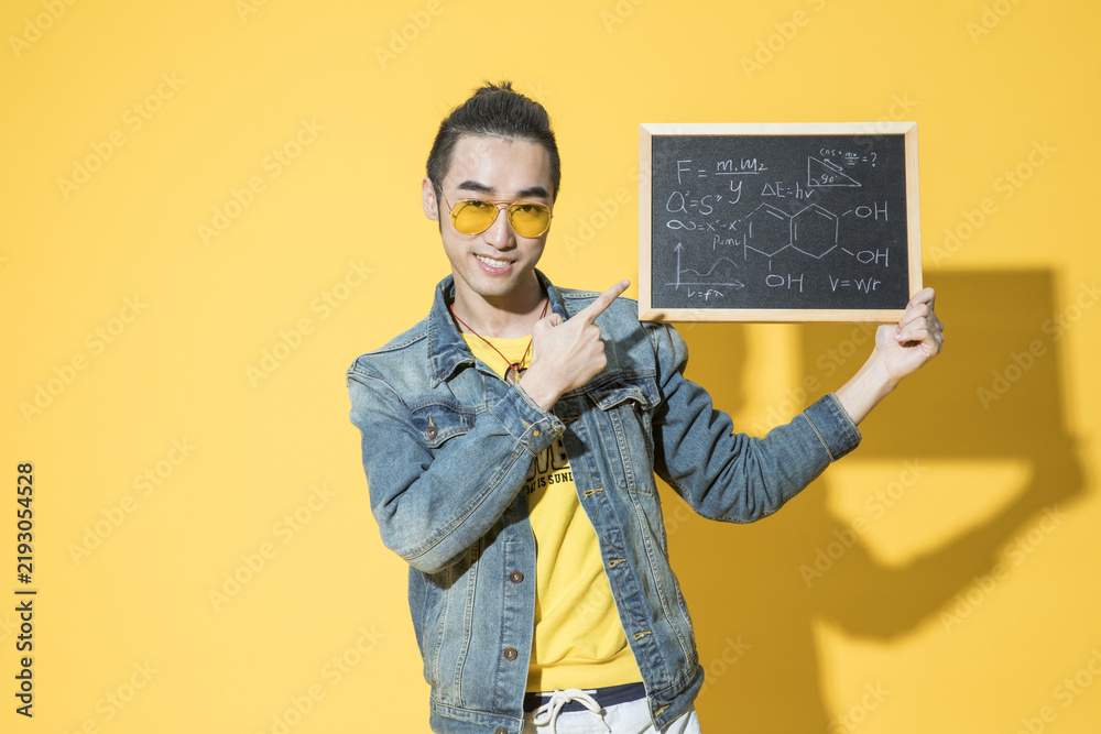Obraz premium Happy young man holding a chalkboard with science formulas on yellow background