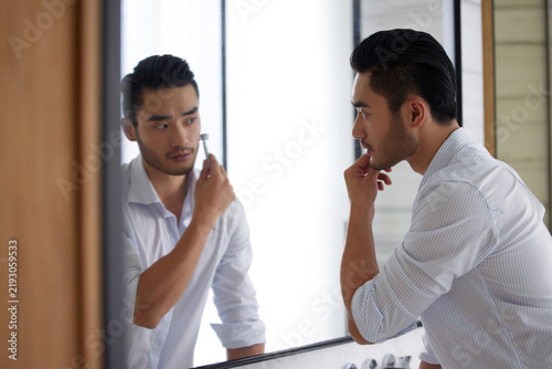 Obraz na plátne Young Man Shaving Facial Hair in Bathroom Mirror