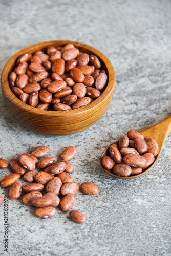 Pinto beans in wooden bowl and spoon on gray concrete background