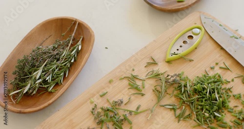 Off-frame trimming is starting as knife and green tool are chopping rosemary and thyme for dish