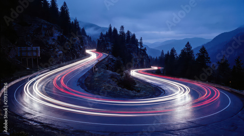 Winding Switchback Mountain Road at Twilight with Circular Red and White Car Light Trails Beneath Forested Hills, Symbolizing Scenic Drive, Adventure Travel and Long Exposure Photography