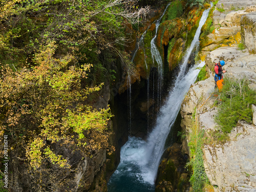 Quadro su tela aerial view of a serene waterfall in a canyon with lush vegetation and climbing gear-wearing individuals enjoying outdoor recreation and canyoning activities under