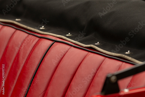 Close-up view of a red ribbed leather car seat and adjacent black convertible top fabric. Visible details include stitched vertical seams, contrasting black