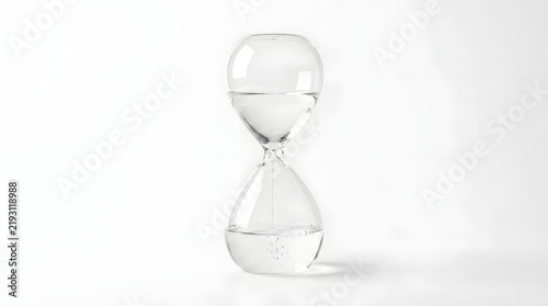 An elegant transparent hourglass filled with liquid  showing water descending through its narrow neck into the lower bulb on a minimalist white surface