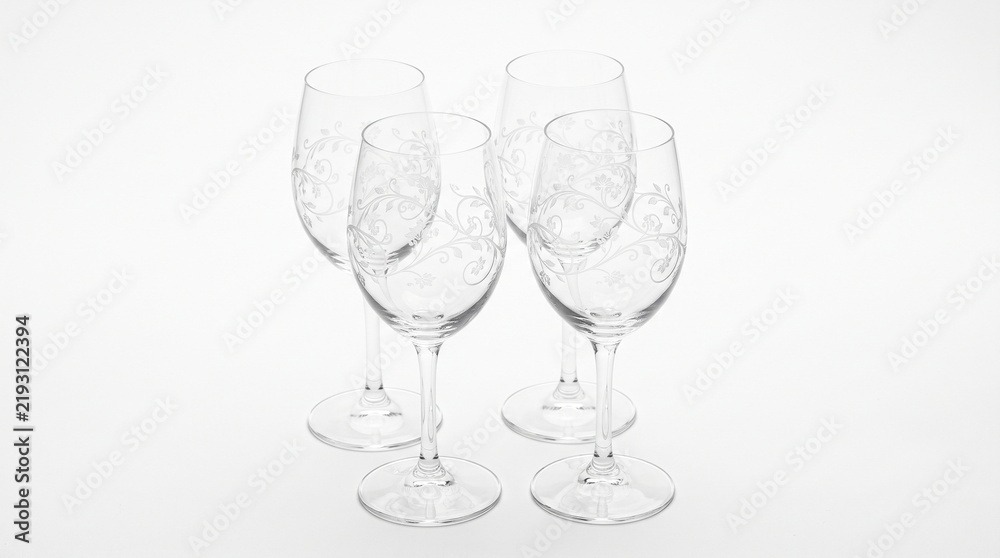 Fototapeta premium Four clear wine glasses with etched floral patterns arranged on a white background