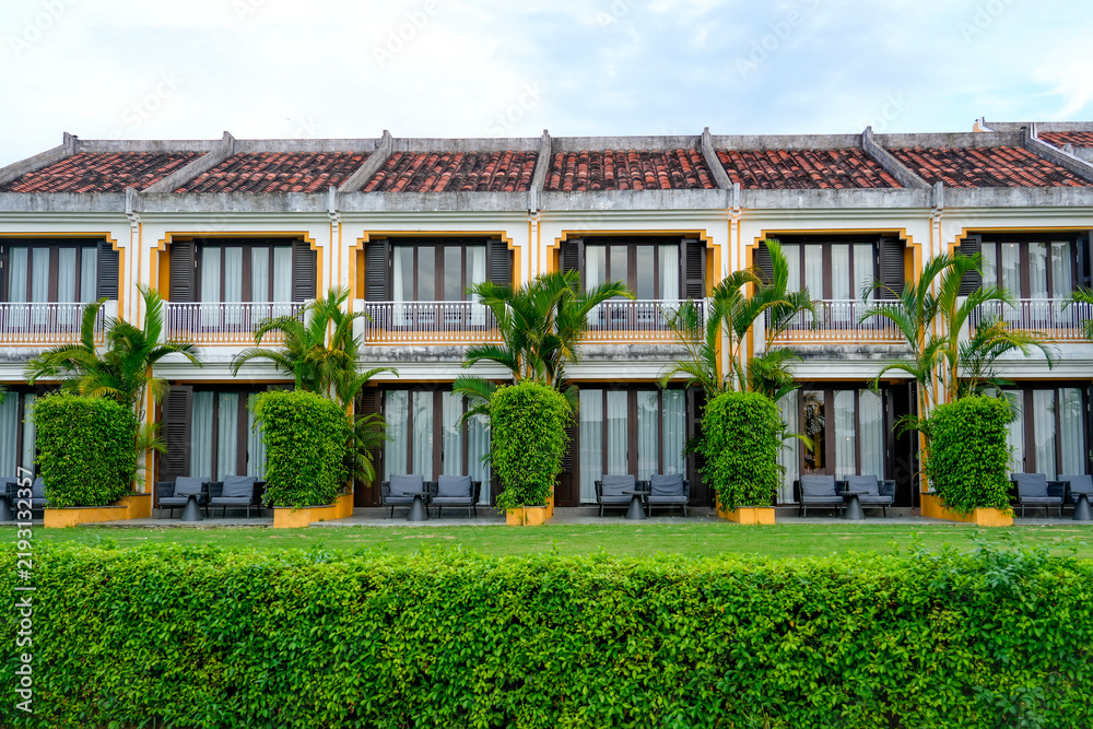 Fototapeta premium Bright facade of a traditional building in Vietnam displays charming balconies and neatly manicured shrubs during a serene afternoon retreat