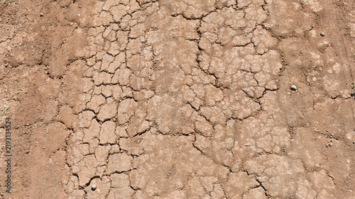 Фотография Cracked dry red clay earth texture of a parched road surface under bright sunlight