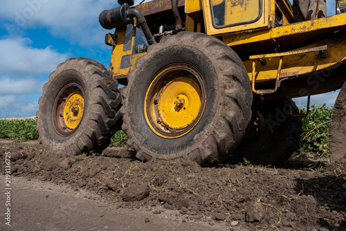 Konstfotografi Low angle view of rear wheels on a yellow motor grader working on dirt road